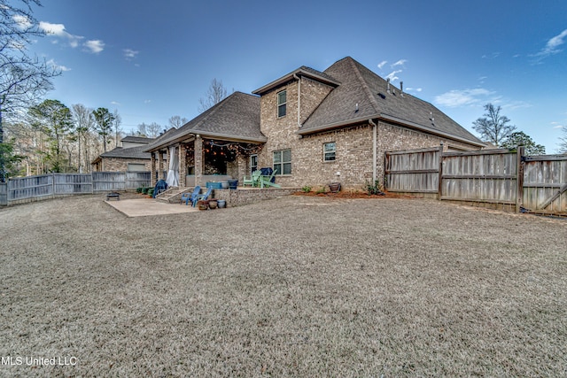 rear view of house featuring brick siding, a patio, a fenced backyard, and roof with shingles