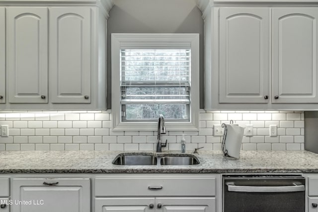 kitchen with dishwashing machine, light stone counters, a sink, white cabinets, and backsplash