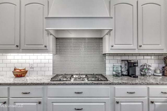 kitchen featuring white cabinets, premium range hood, stainless steel gas stovetop, and backsplash