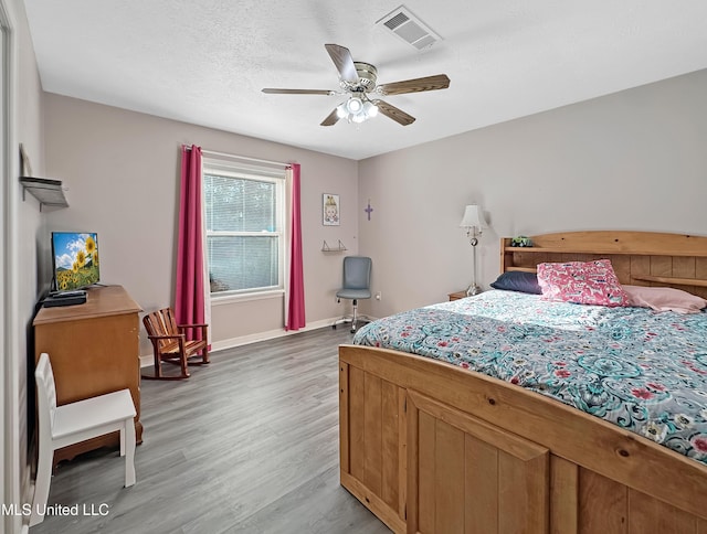 bedroom featuring light wood finished floors, baseboards, visible vents, a ceiling fan, and a textured ceiling