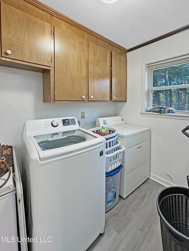 clothes washing area with a textured ceiling, separate washer and dryer, light wood finished floors, and cabinet space