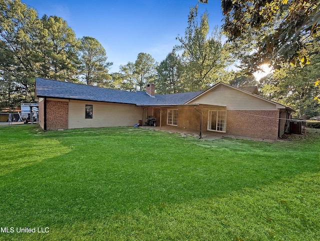 rear view of house featuring a chimney, a lawn, and brick siding