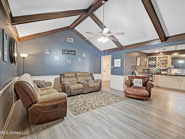 living room featuring light wood-type flooring, wet bar, wainscoting, and visible vents