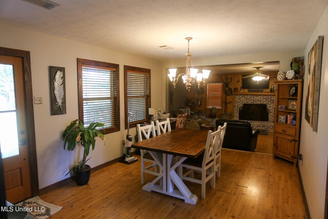 dining room with light hardwood / wood-style floors, ceiling fan with notable chandelier, and a brick fireplace