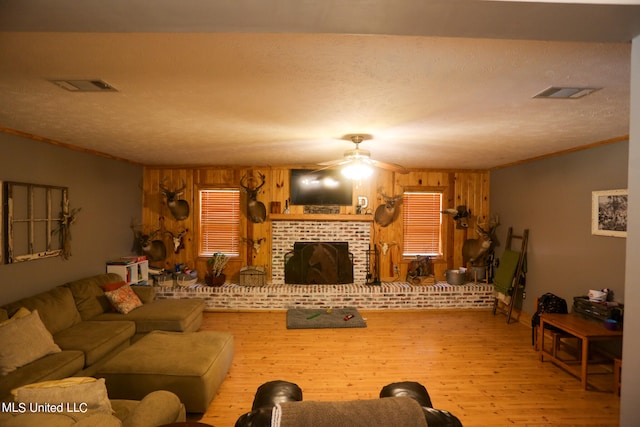 living room featuring wood walls, a fireplace, light hardwood / wood-style floors, ceiling fan, and ornamental molding