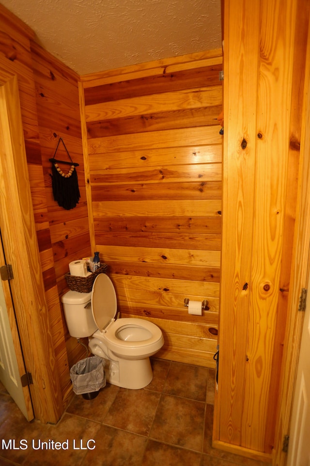 bathroom featuring tile patterned floors, a textured ceiling, toilet, and wood walls