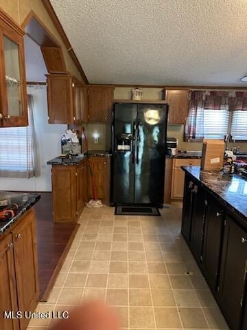 kitchen with brown cabinetry, black fridge, a textured ceiling, and glass insert cabinets