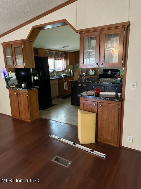kitchen featuring dark countertops, visible vents, black fridge with ice dispenser, crown molding, and dark wood-type flooring