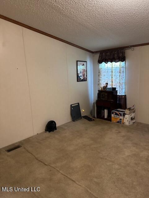 interior space with a textured ceiling, carpet, visible vents, and ornamental molding