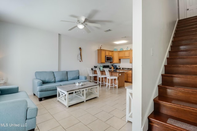 living area with light tile patterned floors, visible vents, stairs, and ceiling fan