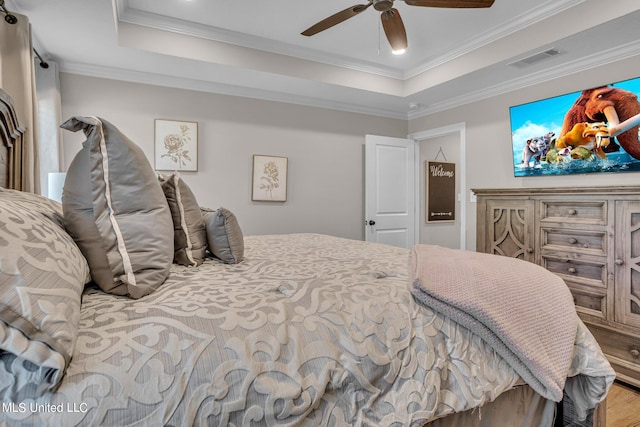 bedroom with crown molding, hardwood / wood-style floors, a tray ceiling, and ceiling fan