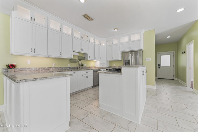 kitchen featuring a kitchen island, appliances with stainless steel finishes, white cabinetry, sink, and light stone countertops