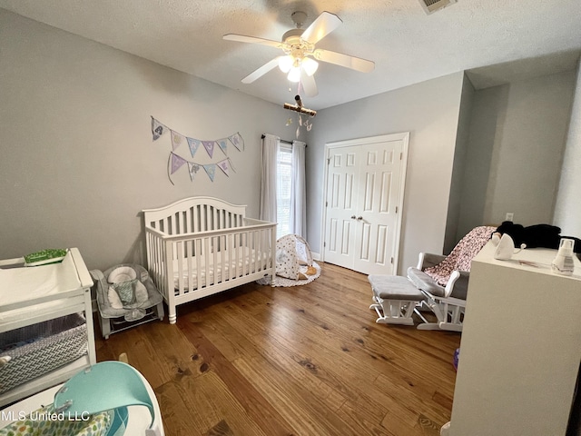 bedroom featuring hardwood / wood-style floors, ceiling fan, a crib, a textured ceiling, and a closet