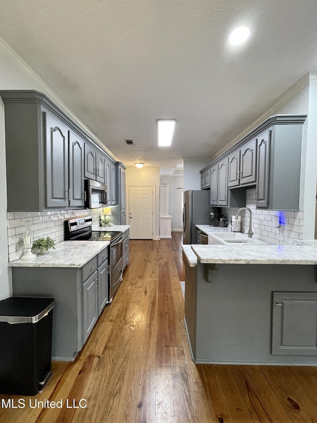 kitchen with sink, gray cabinetry, wood-type flooring, kitchen peninsula, and stainless steel appliances