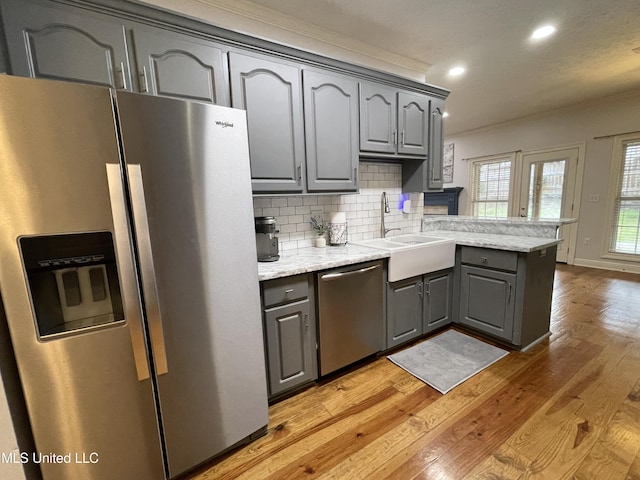 kitchen with gray cabinetry, light hardwood / wood-style flooring, stainless steel appliances, and kitchen peninsula