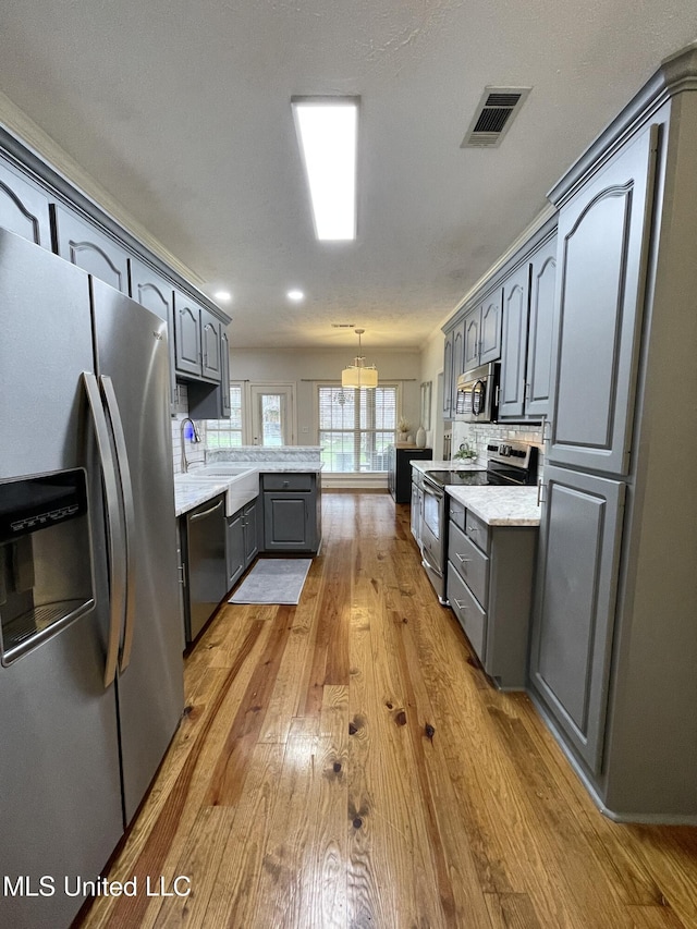 kitchen with gray cabinets, appliances with stainless steel finishes, sink, hanging light fixtures, and light hardwood / wood-style floors