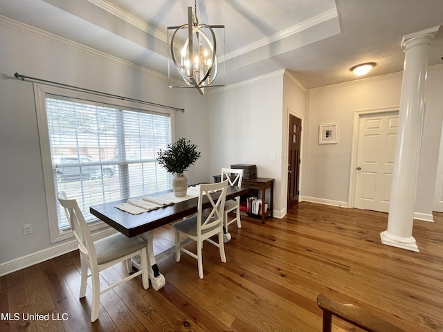 dining room featuring dark wood-type flooring, ornamental molding, a raised ceiling, and ornate columns