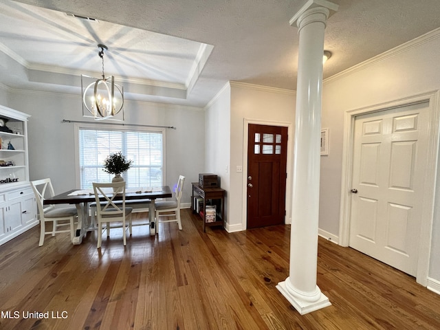 dining space featuring dark wood-type flooring, an inviting chandelier, decorative columns, a tray ceiling, and ornamental molding