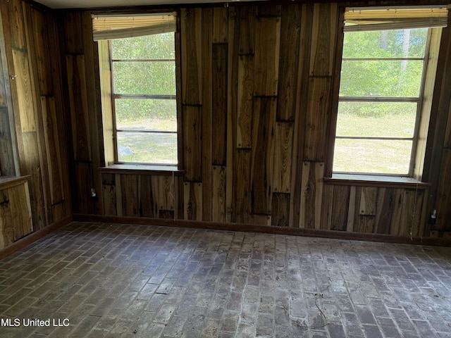 empty room with wooden walls, brick flooring, and healthy amount of natural light