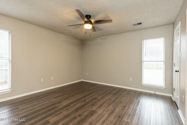 empty room featuring a healthy amount of sunlight, visible vents, ceiling fan, and dark wood-style flooring