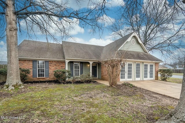 view of front of home with french doors, brick siding, roof with shingles, driveway, and a front lawn