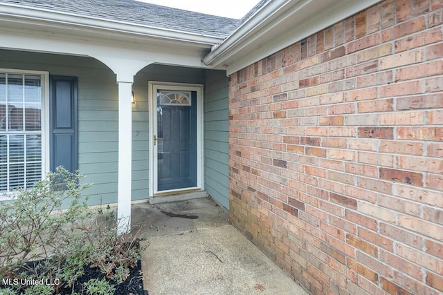 entrance to property with roof with shingles and brick siding