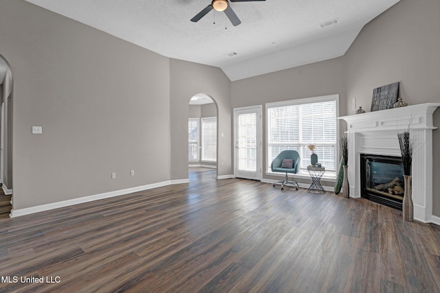 unfurnished living room with arched walkways, vaulted ceiling, dark wood finished floors, and a glass covered fireplace