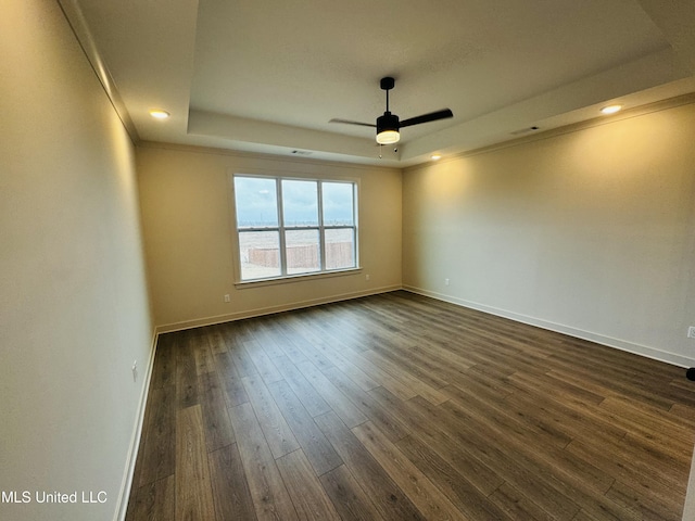 empty room featuring a tray ceiling, dark hardwood / wood-style floors, and ceiling fan