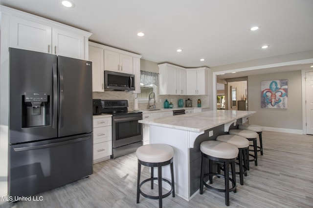 kitchen with stainless steel appliances, sink, light hardwood / wood-style flooring, white cabinets, and a kitchen island