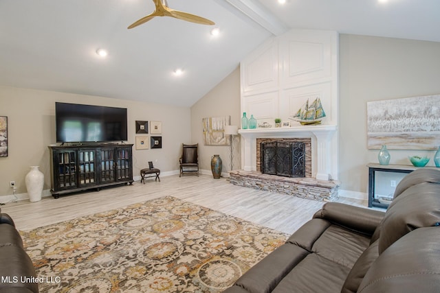 living room featuring lofted ceiling with beams, ceiling fan, a stone fireplace, and wood-type flooring