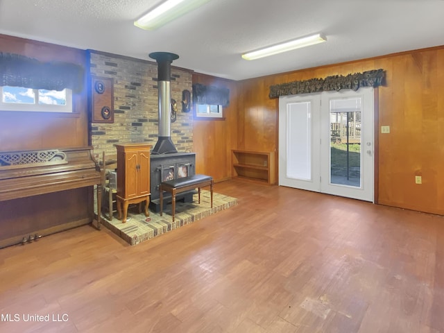 living room with light hardwood / wood-style flooring, wood walls, a wood stove, and a textured ceiling