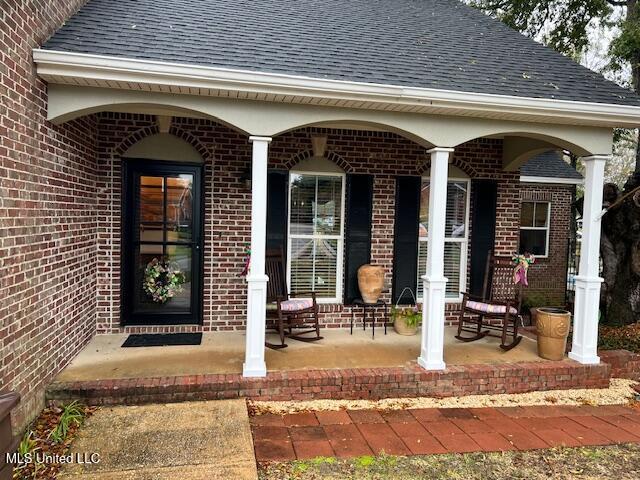 doorway to property with covered porch, roof with shingles, and brick siding