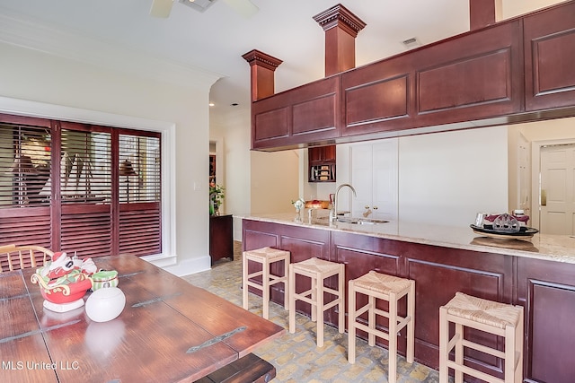 kitchen featuring ornate columns, light stone countertops, sink, and crown molding