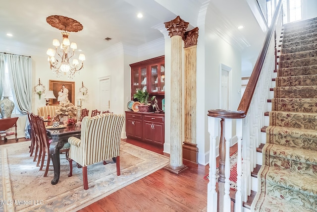 dining space with hardwood / wood-style floors, an inviting chandelier, crown molding, and ornate columns