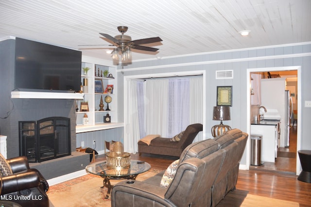 living room featuring ceiling fan, sink, a brick fireplace, wood-type flooring, and ornamental molding