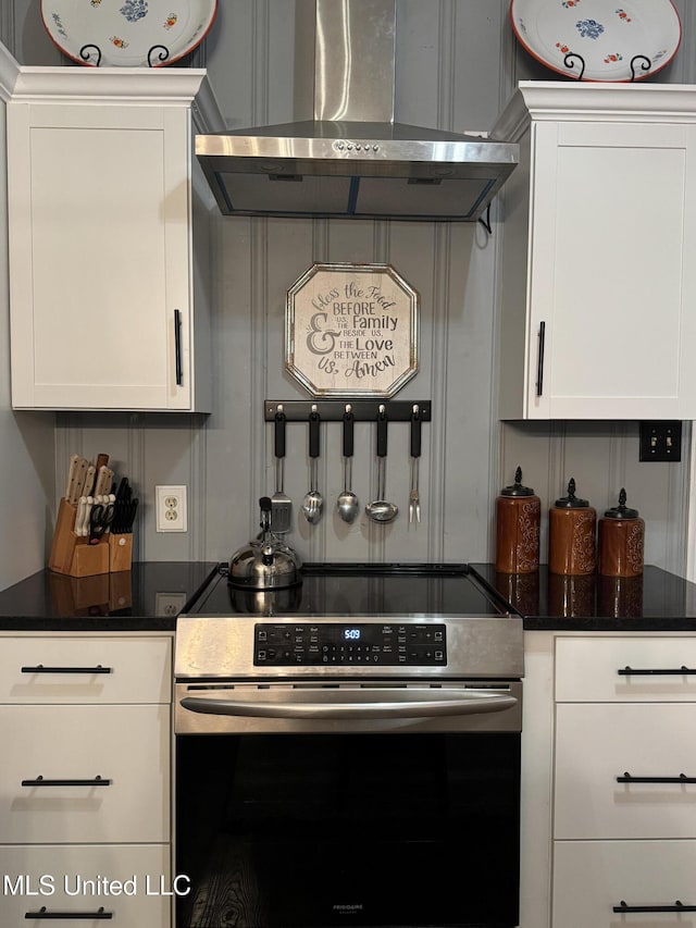 kitchen with white cabinetry, stainless steel electric stove, dark stone counters, and wall chimney range hood