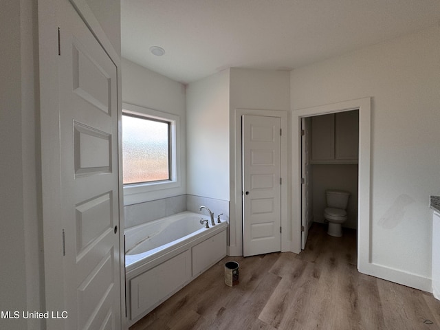 bathroom with toilet, wood-type flooring, and a bath