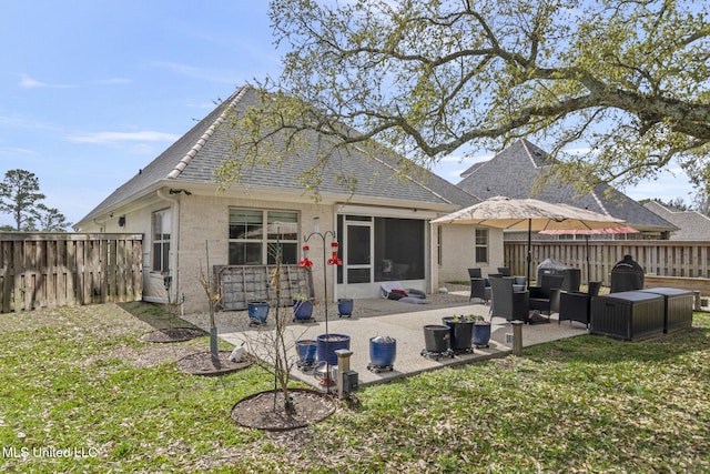 back of house with brick siding, roof with shingles, a yard, a fenced backyard, and a patio area