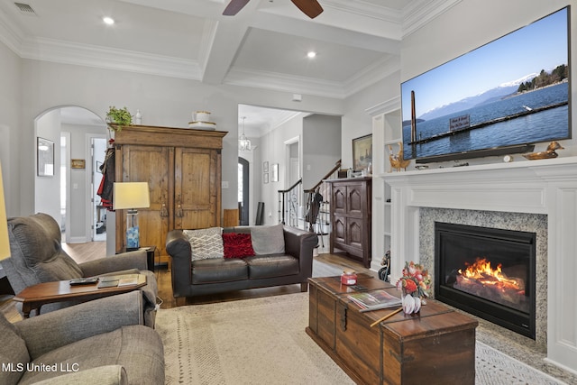 living room featuring stairway, a ceiling fan, arched walkways, light wood-style floors, and beamed ceiling