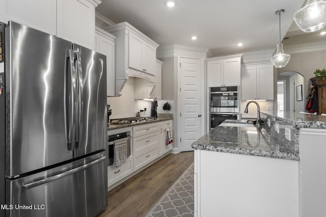 kitchen featuring dark wood finished floors, ornamental molding, appliances with stainless steel finishes, arched walkways, and white cabinetry