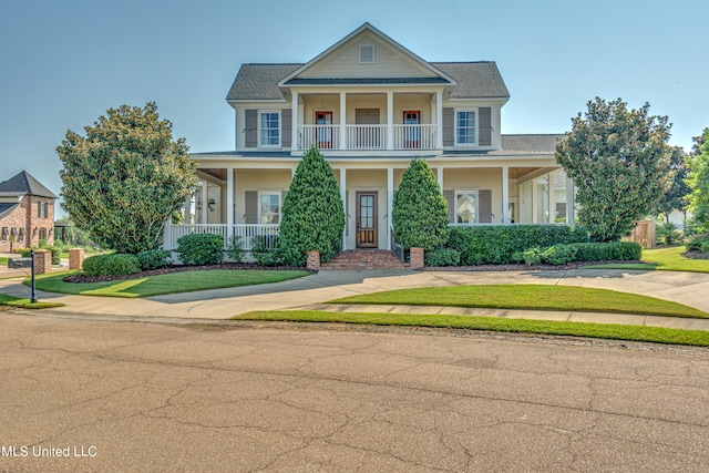 view of front of house with covered porch, a balcony, and a front lawn