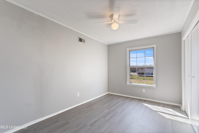 unfurnished bedroom with visible vents, crown molding, wood finished floors, a closet, and a textured ceiling