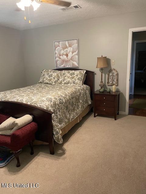 bedroom featuring a textured ceiling, ceiling fan, visible vents, and light carpet