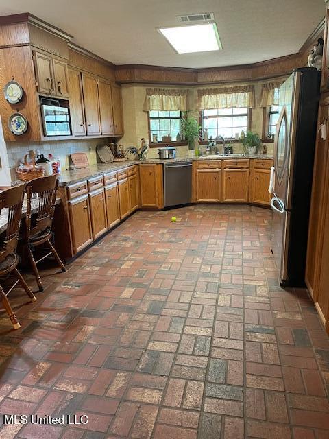 kitchen featuring visible vents, brick floor, a sink, appliances with stainless steel finishes, and brown cabinets