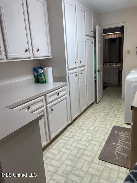 kitchen with brick floor, washer / clothes dryer, white cabinets, and light countertops