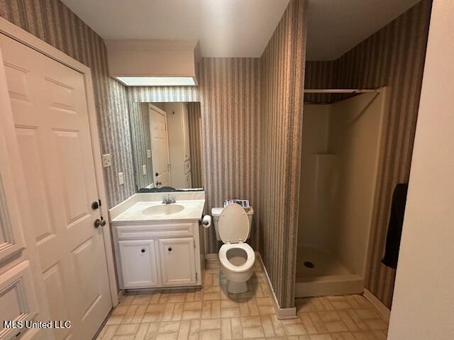 bathroom with wallpapered walls, toilet, vanity, and a stall shower