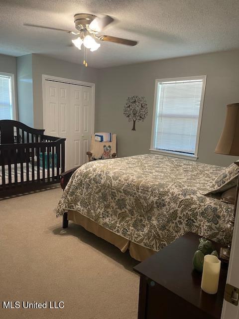 carpeted bedroom with ceiling fan, a closet, and a textured ceiling