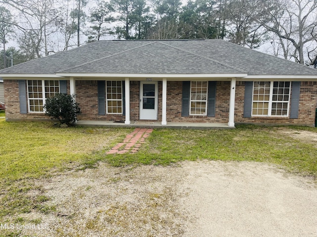 ranch-style house with covered porch, roof with shingles, a front yard, and brick siding