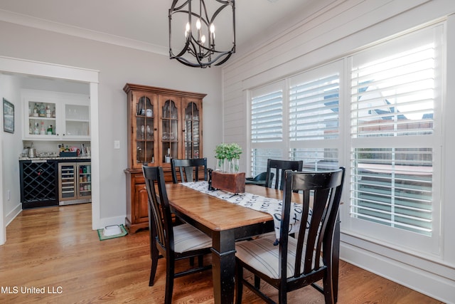 dining space with light wood-type flooring, wine cooler, crown molding, baseboards, and a chandelier