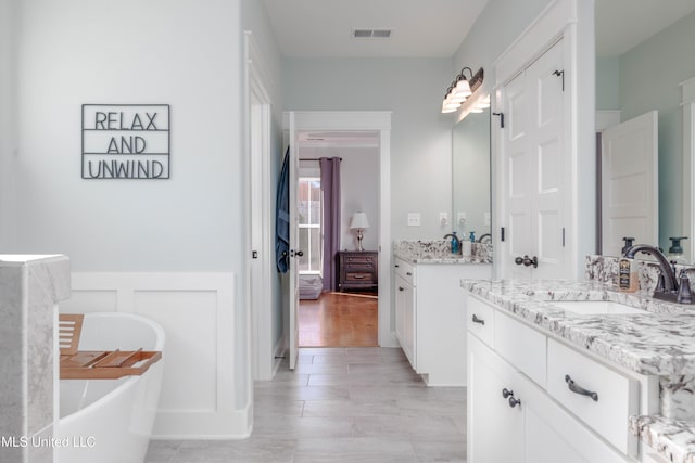 bathroom featuring a sink, visible vents, a freestanding bath, and two vanities